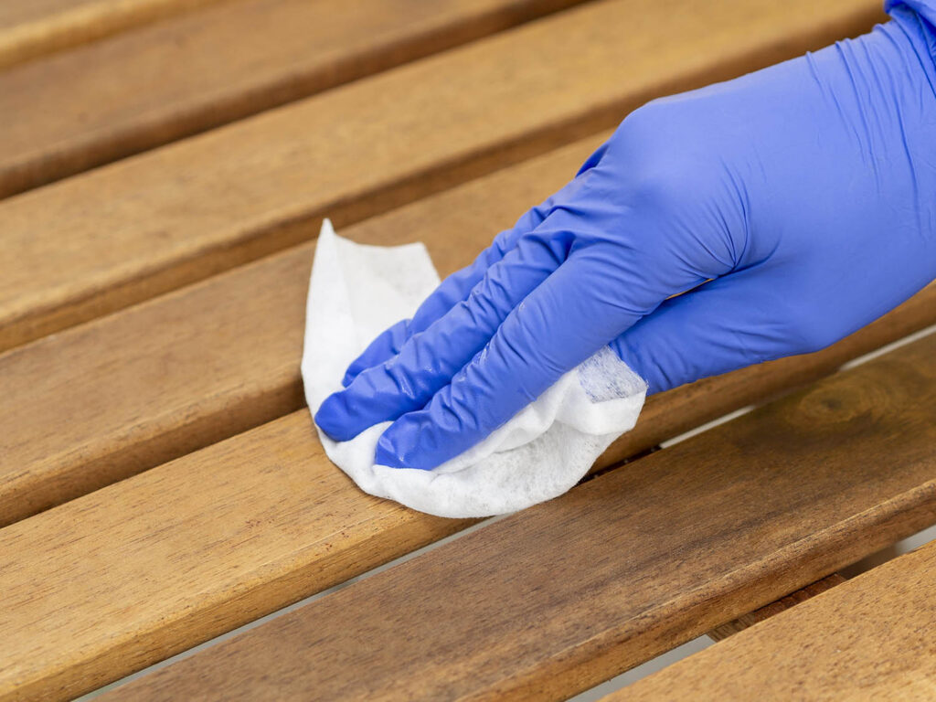 Hand met blauwe handschoen die een wit doekje over hout wrijft.