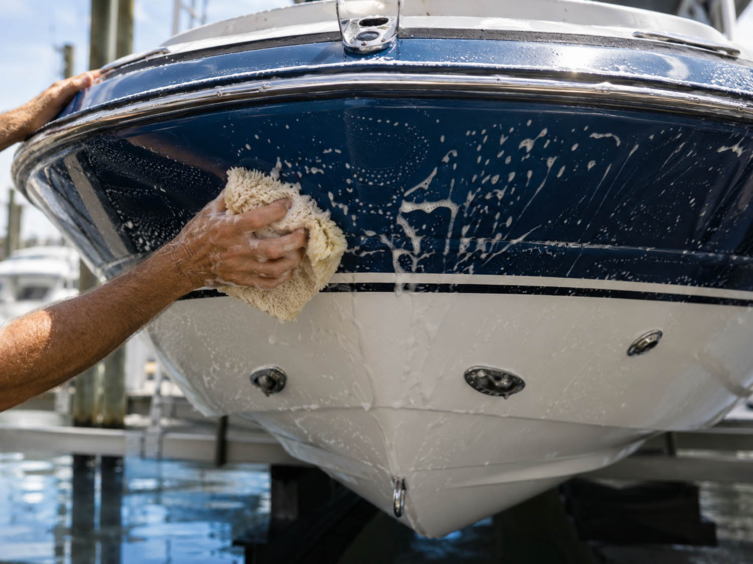 Persoon veegt een donkerblauwe boot schoon met een sponzige doek, zeepachtig schuim op het oppervlak.